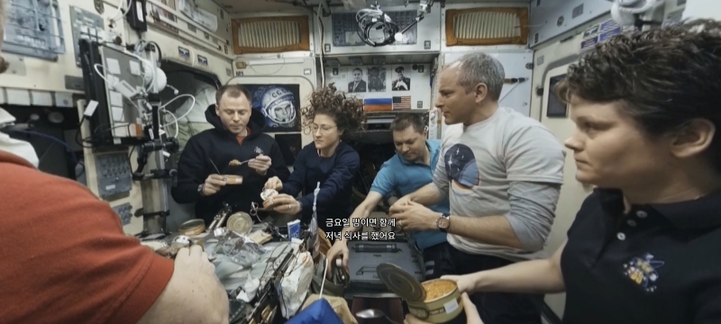 ▲ ISS 우주비행사들이 둘러 앉아 식사를 하는 모습, 무중력 상태를 보여주듯 여성 비행사의 머리가 공중으로 솟구쳐 있다 (자료=ISS 에피소드2 갈무리)